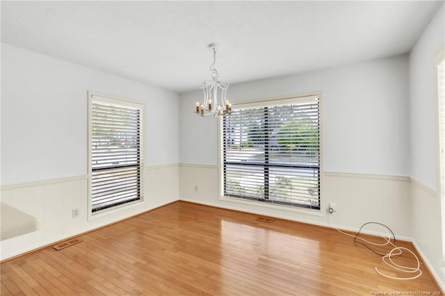 spare room featuring an inviting chandelier, wainscoting, wood finished floors, and visible vents