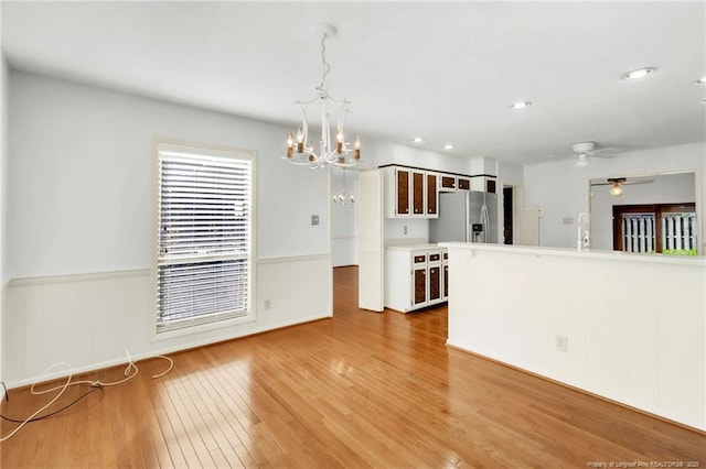 kitchen featuring glass insert cabinets, wainscoting, ceiling fan with notable chandelier, light wood finished floors, and stainless steel refrigerator with ice dispenser