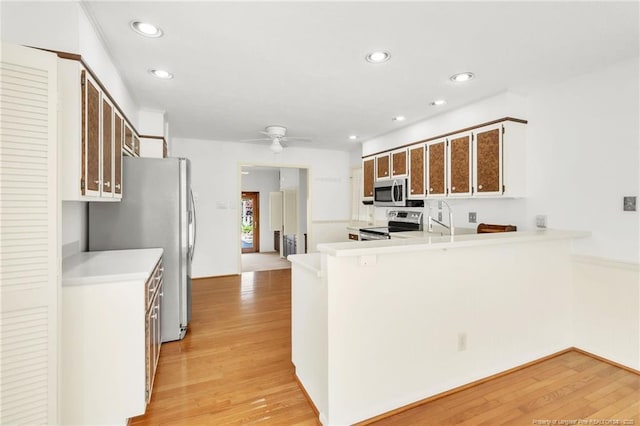 kitchen with stainless steel appliances, a ceiling fan, a peninsula, and light wood finished floors