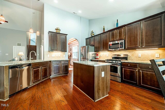 kitchen featuring appliances with stainless steel finishes, high vaulted ceiling, arched walkways, a center island, and dark brown cabinets