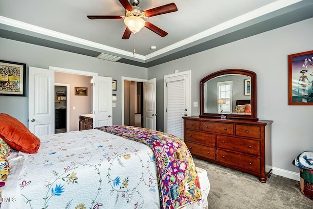 bedroom featuring carpet floors, a tray ceiling, baseboards, a ceiling fan, and ensuite bath