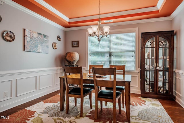 dining area with a raised ceiling, dark wood-style floors, a chandelier, crown molding, and a decorative wall