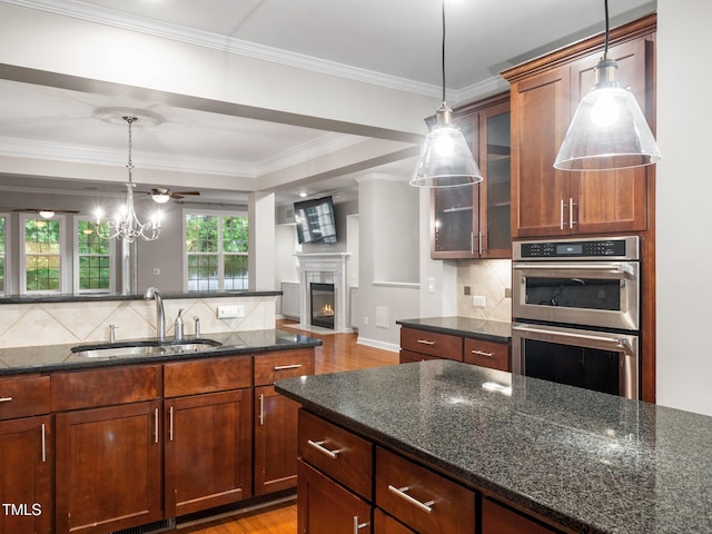 kitchen with glass insert cabinets, a sink, stainless steel double oven, decorative backsplash, and light wood-style floors