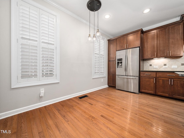 kitchen featuring baseboards, visible vents, stainless steel fridge, crown molding, and tasteful backsplash
