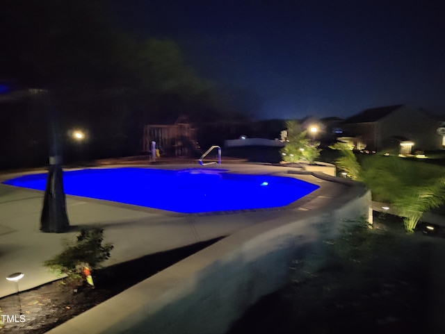 pool at night featuring a patio and an outdoor pool