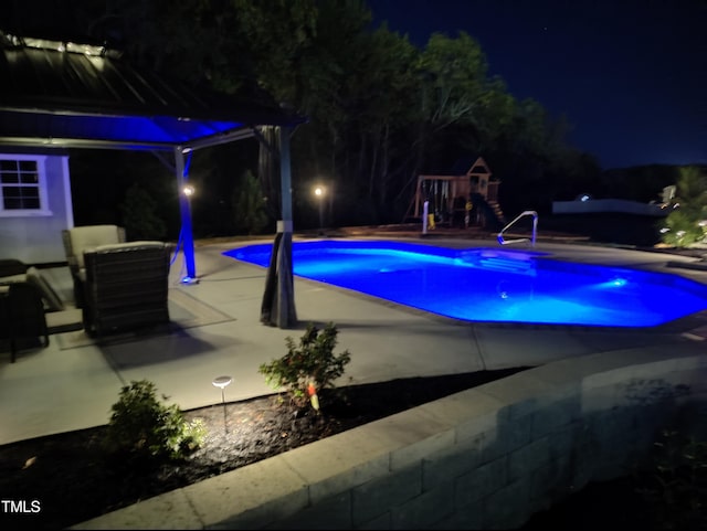 pool at twilight featuring an outdoor pool, a playground, and a patio area