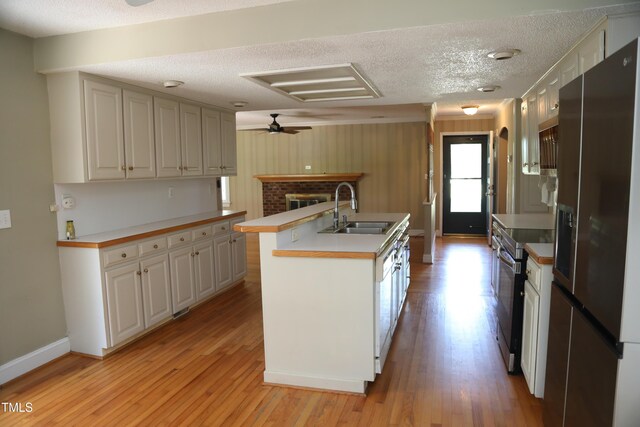 kitchen with a sink, appliances with stainless steel finishes, light wood finished floors, a textured ceiling, and a kitchen island with sink
