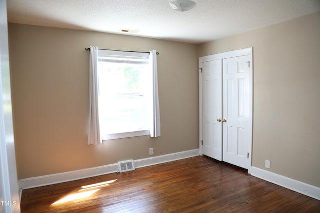 unfurnished bedroom with dark wood-style flooring, a closet, baseboards, and a textured ceiling