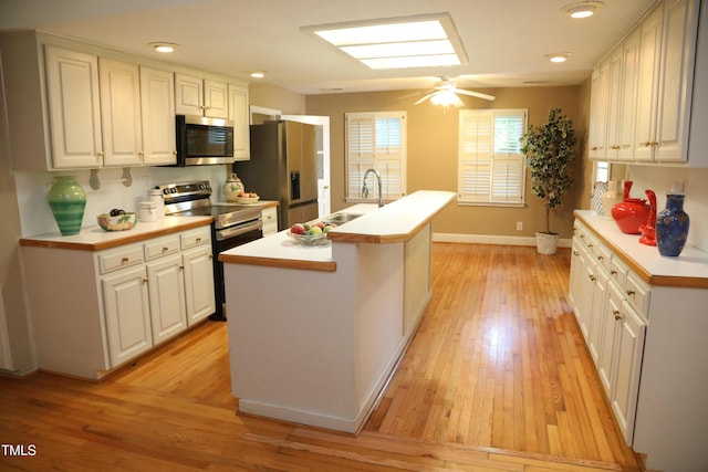1927 Simpkins Rd, Raleigh, NC 27603 - kitchen featuring stainless steel appliances, light wood-style floors, light countertops, white cabinets, and a kitchen island with sink