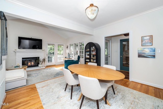 dining room with crown molding, a fireplace, baseboards, wood finished floors, and lofted ceiling