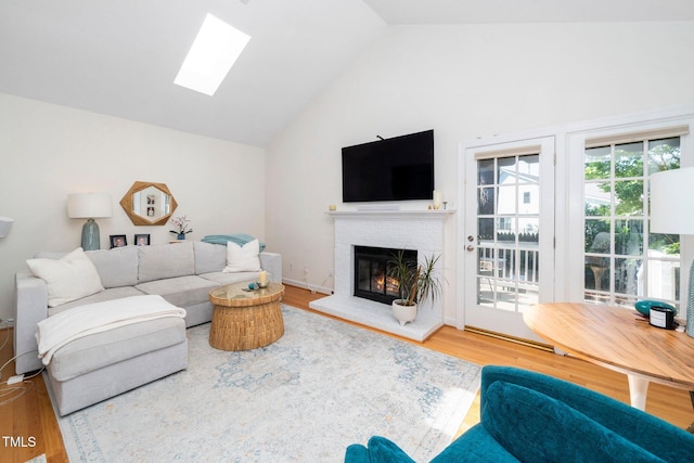living room with a brick fireplace, lofted ceiling with skylight, and wood finished floors
