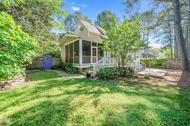 back of house featuring a sunroom, a fenced backyard, a yard, and a storage unit