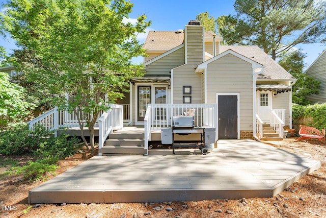 back of property with a wooden deck, a shingled roof, entry steps, and a chimney