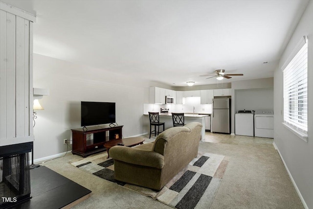living room featuring light carpet, baseboards, a ceiling fan, a multi sided fireplace, and independent washer and dryer