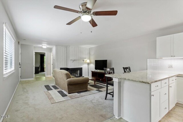 living room with ceiling fan, light carpet, baseboards, and a fireplace
