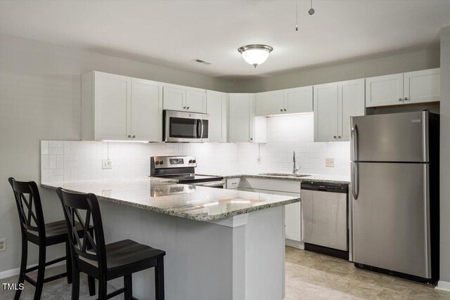 kitchen with light stone countertops, stainless steel appliances, white cabinetry, a peninsula, and backsplash