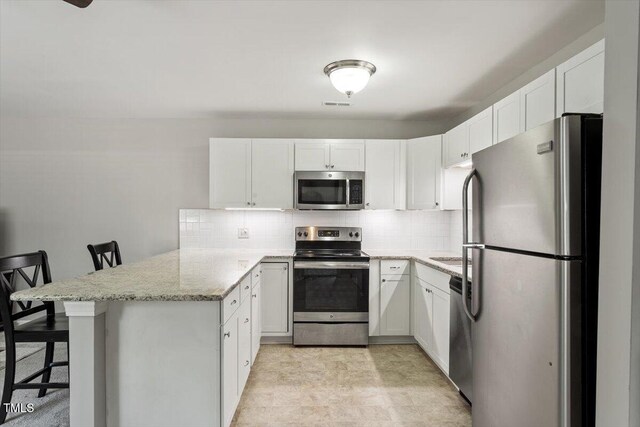 kitchen featuring a peninsula, white cabinetry, tasteful backsplash, light stone counters, and stainless steel appliances