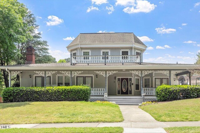 view of front of property featuring a porch, a chimney, a balcony, and a front yard