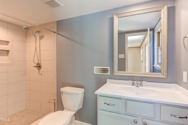 bathroom featuring visible vents, a tile shower, toilet, and vanity