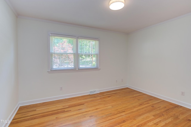 spare room featuring baseboards, ornamental molding, light wood-type flooring, and visible vents