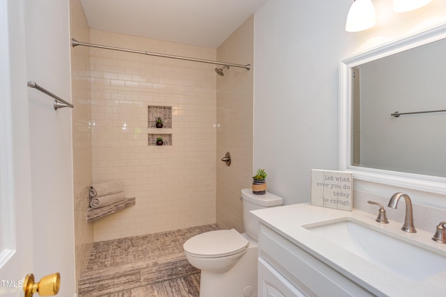 full bath featuring toilet, a tile shower, and vanity