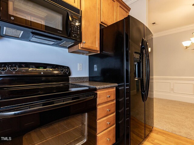 kitchen with crown molding, dark countertops, brown cabinetry, a wainscoted wall, and black appliances