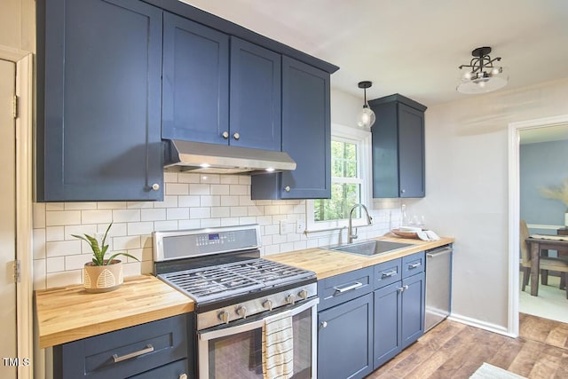 kitchen with appliances with stainless steel finishes, a sink, blue cabinetry, wooden counters, and under cabinet range hood