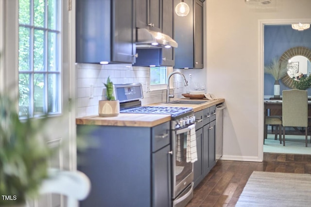 kitchen featuring appliances with stainless steel finishes, tasteful backsplash, a sink, wood counters, and under cabinet range hood