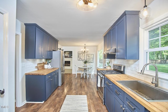 kitchen with wooden counters, appliances with stainless steel finishes, a sink, a notable chandelier, and under cabinet range hood