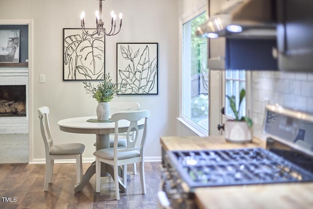 dining room featuring a brick fireplace, baseboards, an inviting chandelier, and wood finished floors