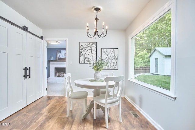 dining room with visible vents, wood finished floors, baseboards, a barn door, and a chandelier
