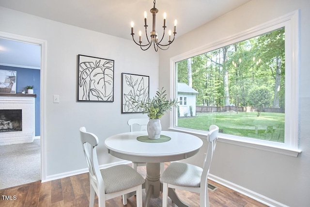 dining space with an inviting chandelier, baseboards, a brick fireplace, and wood finished floors