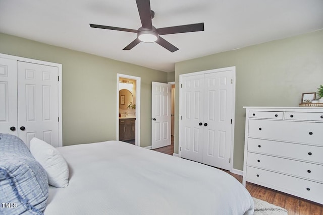 bedroom featuring a ceiling fan, dark wood-style flooring, baseboards, multiple closets, and ensuite bath
