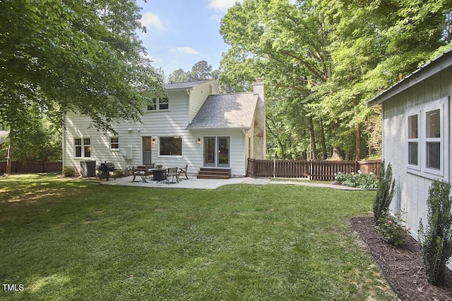 back of property with entry steps, a fenced backyard, a chimney, a patio, and a yard