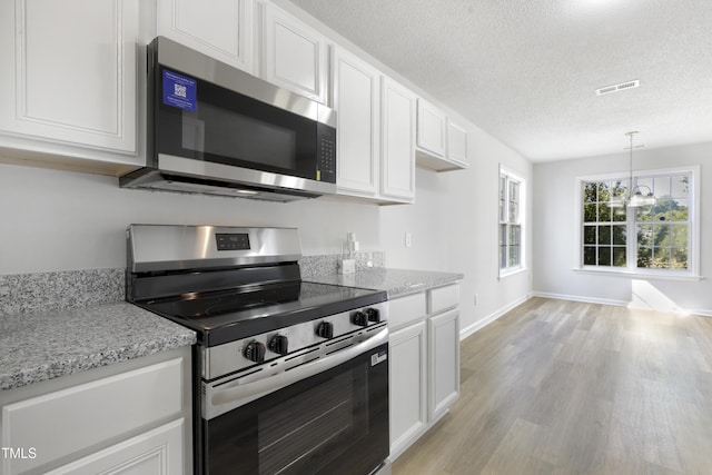 kitchen with appliances with stainless steel finishes, white cabinets, light wood finished floors, and a textured ceiling