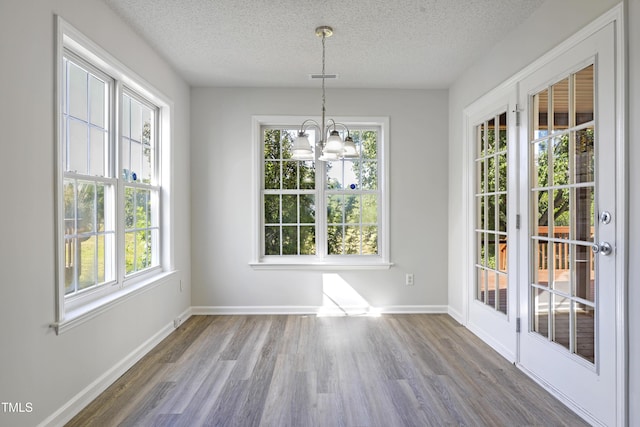 unfurnished dining area with an inviting chandelier, a textured ceiling, plenty of natural light, and wood finished floors