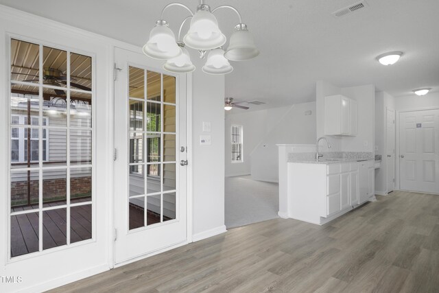 kitchen with visible vents, light stone countertops, light wood-style floors, white cabinets, and a sink