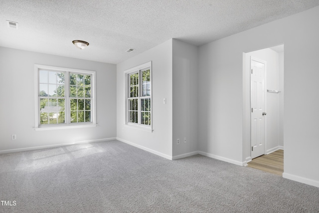 empty room with a textured ceiling, baseboards, visible vents, and carpet