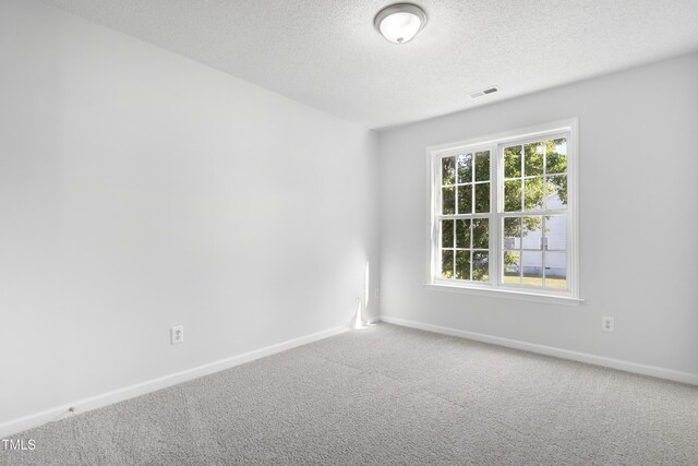 unfurnished room featuring visible vents, carpet, a textured ceiling, and baseboards