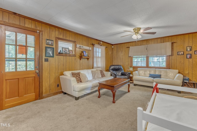 living room featuring carpet floors, wooden walls, ceiling fan, and crown molding