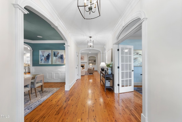 foyer with arched walkways, a chandelier, wood finished floors, crown molding, and a wainscoted wall
