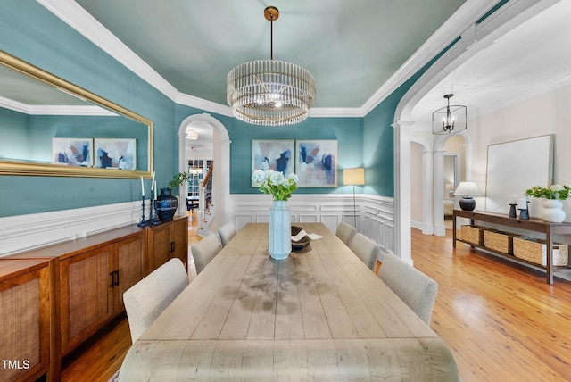 dining room with a chandelier, arched walkways, a wainscoted wall, wood finished floors, and ornamental molding