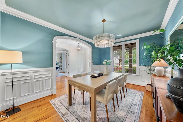 dining space with arched walkways, a chandelier, crown molding, wainscoting, and light wood finished floors