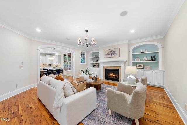 living room with arched walkways, a chandelier, light wood-style floors, baseboards, and ornamental molding