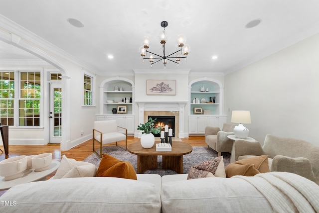 living room featuring baseboards, light wood-style floors, built in shelves, a chandelier, and a glass covered fireplace