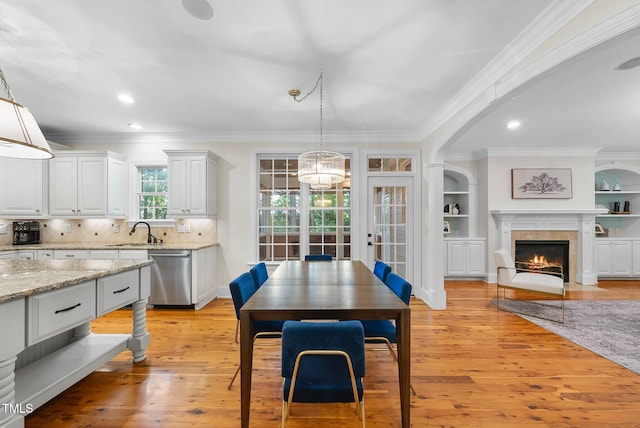 kitchen with dishwasher, crown molding, light wood-style floors, decorative light fixtures, and light stone counters