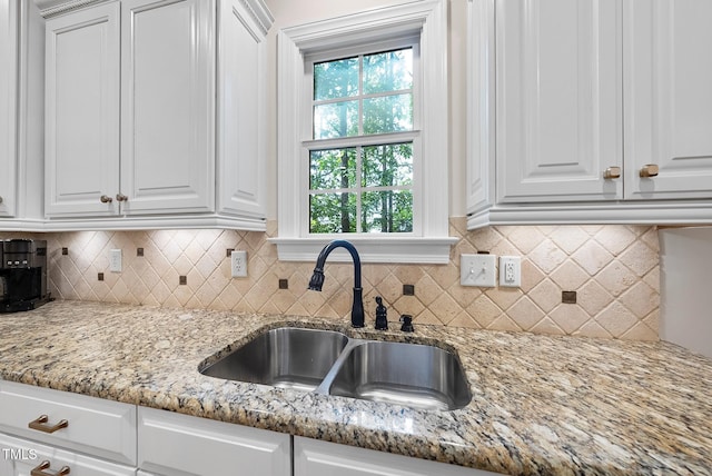 kitchen featuring a sink, white cabinets, and light stone countertops