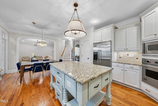 kitchen with built in appliances, arched walkways, white cabinets, light wood-style floors, and ornamental molding