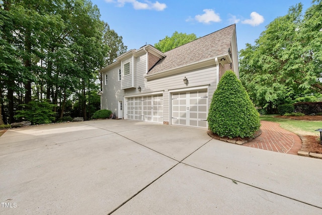 view of side of property featuring driveway, roof with shingles, and an attached garage