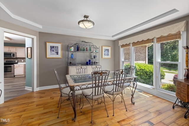dining area featuring baseboards, a raised ceiling, and light wood-type flooring